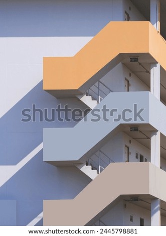 Geometric zigzag pattern of multicolored fire escape outside of apartment building in vertical frame with sunlight and shadow on surface, exterior architecture background in minimal style