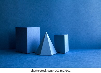 Geometrical figures still life composition. Three-dimensional prism pyramid tetrahedron rectangular cube objects on blue background. Platonic solids figures, simplicity concept photography.
