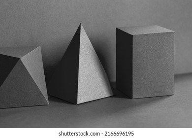 Geometrical figures still life composition. Three-dimensional prism pyramid tetrahedron rectangular cube objects on black gray background. Platonic solids figures, simplicity concept photography.