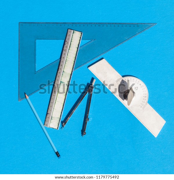 Geometry set with compass, rulers, pencil and\
protractor on blue background - top\
view