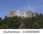 George Washington is highlighted with sun shining on his face at Mount Rushmore. Father of our country is distinguished looking on top of mountain.