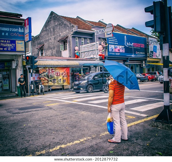 Georgetown\
Penang Malaysia November 11 2017. Man holding a blue umbrella on\
the street in Georgetown Penang. People waiting at a zebra crossing\
in Asia. Old buildings in the background.\
