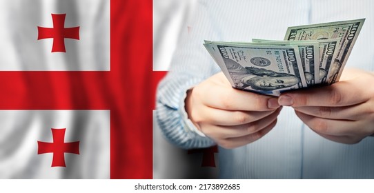 Georgian Flag And US Dollars In Hands. Business, Tax, Banking And Finance Concept