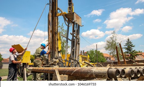 Geothermal Drillers at Work.
Drilling geothermal well for a residential geothermal heat pump. Geothermal water well drilling equipment. Workers lifting a drill pipe on a drilling rig.
