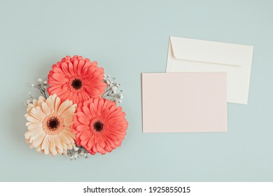 Gerbera Flowers With Blank Card And Envelopes Over Light Green Background. Easter Holiday, Mothers Day Greeting Card Concept