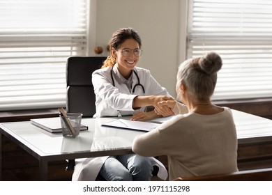 Geriatric Medicine. Smiling Young Hispanic Female Doctor Shake Hand Of Elderly Woman Patient Greet With Recovery Good Result Of Therapy. Mature Old Lady Handshake With Doc Gp Appreciate For Help Care