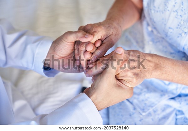 A geriatric nurse or doctor\
holds the hands of a senior citizen as a symbol of support and\
comfort