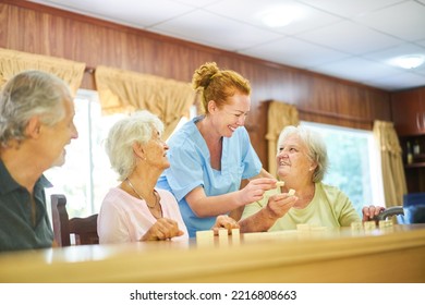 Geriatric Nurse Helping Senior With Dementia Play Dominoes At Game Night In Nursing Home