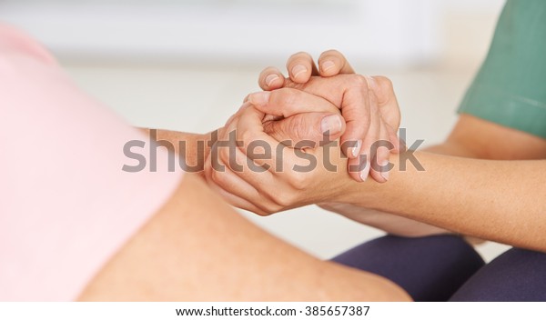 Geriatric nurse holding hands of senior woman\
for consolation