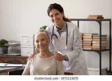 Geriatric patient. Smiling millennial hispanic female doctor embracing shoulders of happy mature lady at office in clinic. Portrait of attending physician and senior woman visitor looking at camera - Shutterstock ID 1971115070