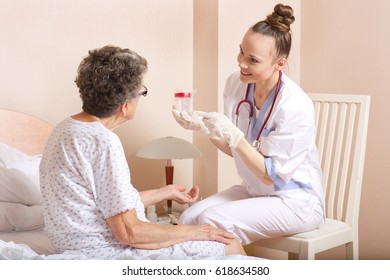 Geriatrician visits a senior woman between 70 and 80 years old in her ward  Medical sister gives a collection cup for urine to a senior woman