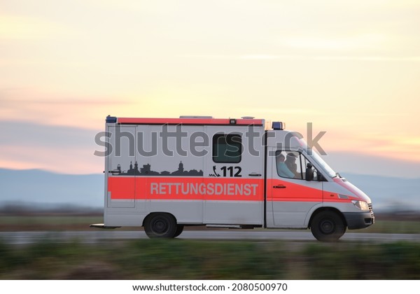 German ambulance van driving fast in\
road in evening. Berlin, Germany - March 5 12,\
2021.