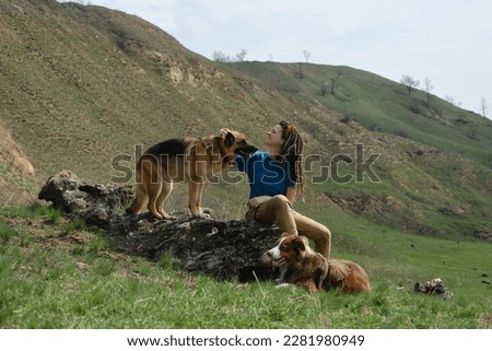 German and Australian Shepherd are companion dogs. Hiking in mountains with pets. Young Caucasian woman sitting on hill with two dogs in spring and enjoying views of nature.