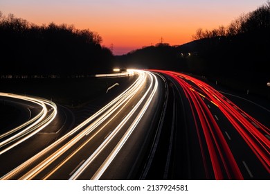 German Autobahn A46 At Dusk On A Winter Evening In Iserlohn Sauerland At Junction Driveway Town Centre, Long Time Exposure With Light Traces Of Passing Car Lights. Orange Sky Gradient After Sunset.