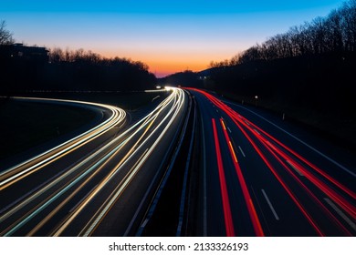 German Autobahn A46 At Evening Twilight In Winter In Iserlohn Sauerland At Junction Driveway Town Centre, Long Time Exposure With Light Traces Of Passing Car Lights. Colorful Blue Sky Gradient.