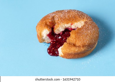 German Berliner doughnut with raspberry jam filling on a blue seamless background. Macro image of a donut with jam. Homemade dessert. Famous sweets.