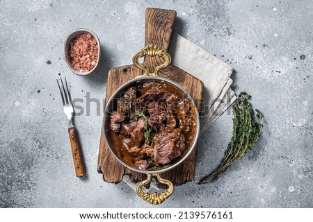 German braised beef cheeks in brown red wine sauce. Gray background. Top view.