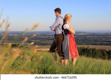 A German Couple In Bavarian Costume Back To Back On Grass