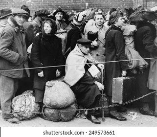 German displaced persons wait in Berlin's Anhalter Station in 1945. Refugees are carrying their few belongings, as the stand behind a rope and double strand of barbed wire.