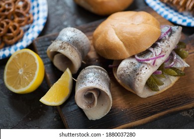 German Fish Sandwich With Herring Filet, Pickles, Red Onion And Lemon On A Rustic Wooden Cutting Board, Closeup
