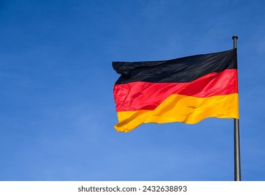 German flag flying on the wind. Waving flag of Germany on flagpole against blue sky. Deutschland. Black, red and yellow colors on German flag in a front of Bundestag. Symbol of German people.  - Powered by Shutterstock