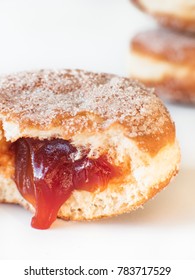 German fried donut, so called Krapfen, Berliner or Pfannkuchen, filled with rose hip jam and dusted with cinnamon sugar, traditionally eaten at carnival and at New Year's Eve on white background