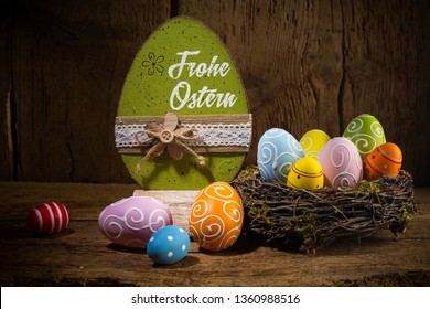 German greetings Frohe Ostern ( english translation happy easter ) Colorful painted eggs in birds nest basket on rustic wooden old  greeting card background