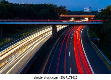 German Motorway Crossing In Dortmund. Junction At Dusk With Light Traces Of Passing Fast Cars And Blue Evening Sky. Long Time Exposure From A Bridge Above The Highway With White And Red Lights.