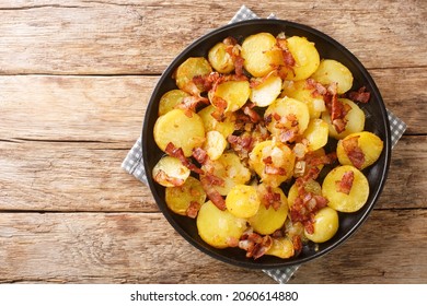 German Pan Fried Potatoes or Bratkartoffeln With Bacon and Onion close up in the plate on the table. Horizontal top view from above