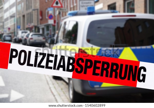 German police car in the city standing behind cordon\
tape with the word „Polizeiabsperrung“, the German word for police\
cordon 