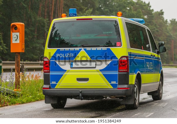German police car on a motorway in the state of\
Brandenburg from a side view. Emergency telephone in an emergency\
bay on the side of the road. two-lane highway with asphalt surface\
in rainy weather