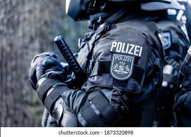 A german police officer is waiting in his riot body protection on a demonstration against the corona-laws. He has a tonfa or baton in his hand and a coat of arms of the city of Bremen on a badge.