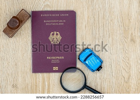 German Republic passport on a wooden table, a miniature car and a magnifying glass. Search concept for business and holiday travels