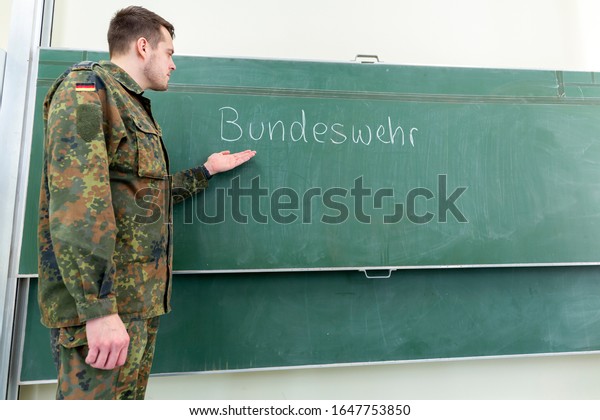 German soldier stands in a classroom .\
German word Bundeswehr, means german\
army.
