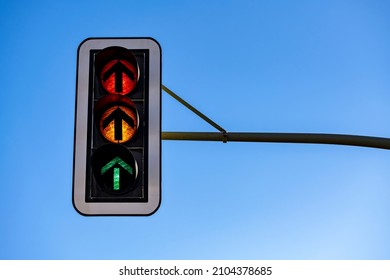 German traffic lights “Ampel“ with all three flashlights shining simultaneously isolated on blue sky. Red, orange or yellow, green light with arrows indicating “straight ahead“, hanging above crossing - Shutterstock ID 2104378685