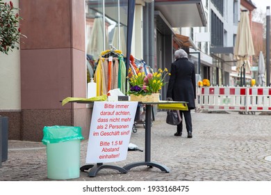 German Warning Sign In Front Of A Boutique, Antiseptic Disinfection Stands For Customers At The Entrance To The Store. Please Aware No More Than 2 People In The Store. Please Keep A Distance Of 1.5 M.