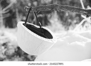 German Wehrmacht Infantry Soldiers White Helmet hanging on wooden banch in snow winter forest. World War II old army equipment ammunition. Metal Helmet Of German Infantry Wehrmacht Soldier At World