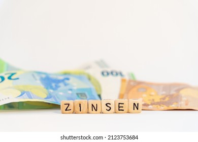 German Word For Interest Charges, ZINSEN, Spelled With Wooden Letters Wooden Cube On A Plain White Background With Banknotes, Concept Image 