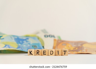 German Word For Loan, KREDIT, Spelled With Wooden Letters Wooden Cube On A Plain White Background With Banknotes, Concept Image 