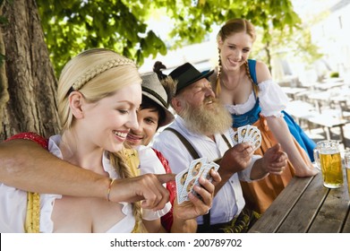 Germany, Bavaria, Upper Bavaria, People In Traditional Costume Playing Cards In Beer Garden