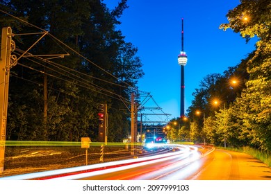 Germany, Cars Passing By Tv Tower And Busy Street Of Stuttgart City In Green Forest Nature Landscape In Magical Evening Twilight Mood After Sunset