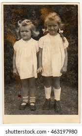 GERMANY - DECEMBER 23, 1946: Vintage photo shows two small girls (siblings). They wear a white dresses. Retro black & whitephotography.