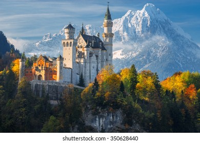 Germany. Famous Neuschwanstein Castle in the background of snowy mountains and trees with yellow and green leaves.