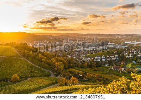 Germany, Stuttgart city panorama view above vineyards, industry, houses, streets, stadium and highway at sunset in warm orange light
