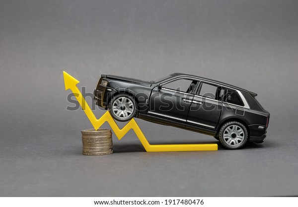 Germany-01.2021 Rising car prices. On a black\
background, there is a model car with a yellow arrow pointing\
upwards. Around the coin. The concept of the growth of the\
transport market and car\
prices.