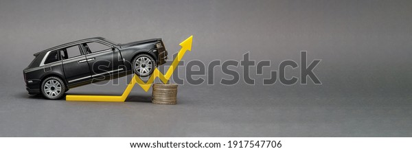 Germany.Hamburg 01.02.2021.Editorial.Rising car\
prices. On a black background, there is a model car with a yellow\
arrow pointing upwards. Around the\
coin.