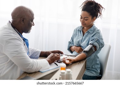 Gestational Hypertension. Mature Male Medical Worker Measuring Arterial Blood Pressure Of Pregnant Black Woman Using Cuff, Patient Having Problems With Tension, Sitting At Table. Health Care Concept