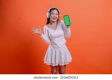 gesture cheerful young ladies woman in white sweater wearing earphone headphone, holding mobile phone screen, cellphone green screen while waving sideways. for entertainment, lifestyle, business - Powered by Shutterstock