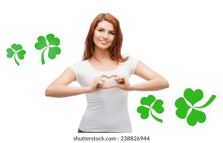 gesture, holidays, st. patricks day and happy people concept - smiling girl in white blank t-shirts showing heart with hands over white background with green shamrock or clover