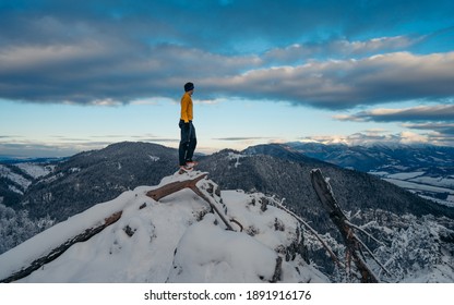Gesture of triumph. Satisfy hiker in yellow shirt and dark trousers. Tall man on the peak of cliff watching down to landscape. Outdoor fashionable clothes